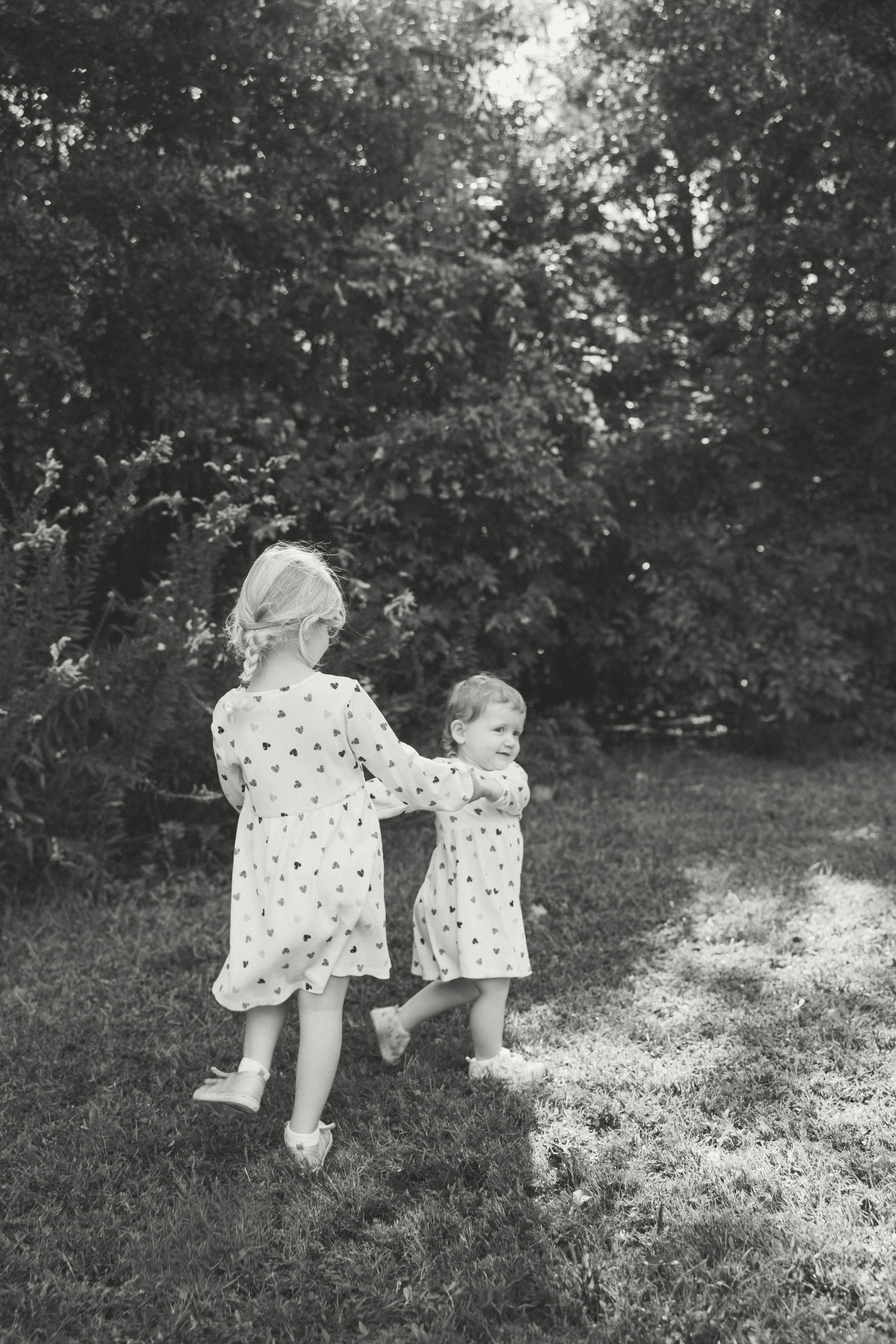 Two children in polka dot dresses bend down to examine something in the grass in this vintage black and white photograph.