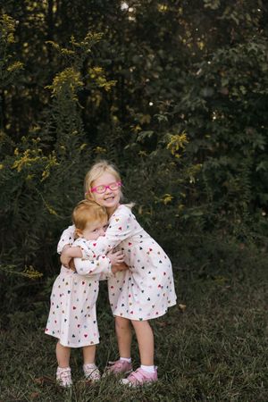 Two young children in matching heart-patterned dresses share sweet moments together outdoors in a series of candid shots.