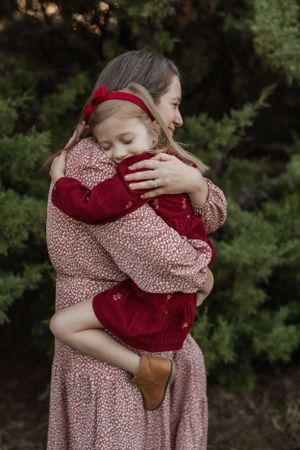 A tender embrace between parent and child wearing red and pink floral patterns against a green outdoor backdrop.