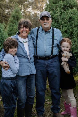 A family group poses together outdoors against evergreen trees with one person wearing suspenders and others in casual attire.