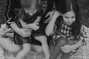 Black and white vintage photograph of two children sitting on a patterned blanket looking down at their hands.
