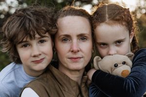 A close-up portrait of three people hugging and smiling together outdoors.