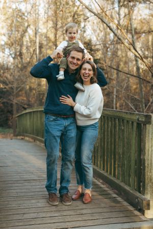 A happy family poses together on a wooden bridge in an autumn forest setting.