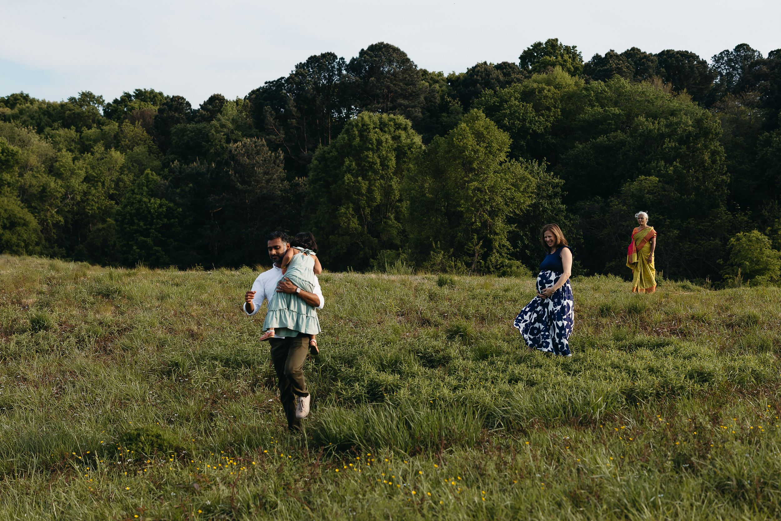 People walking through a lush green meadow with trees in the background on a sunny day.
