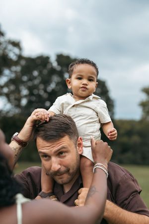 A parent gives their young child a playful shoulder ride outdoors on an overcast day.