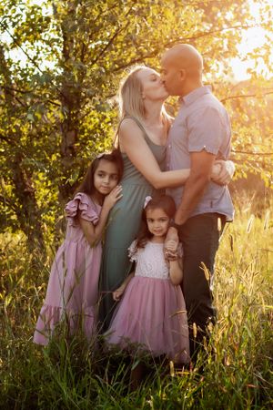 Intimate family portrait in golden sunlight with pink dresses and natural backdrop.