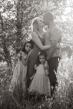 Black and white family portrait in a sun-dappled wooded setting.