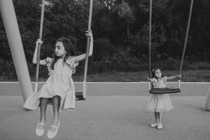 Two children play on swings in a black and white photograph.