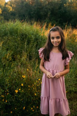 A young girl in a pink ruffled dress poses in a wildflower meadow at sunset.