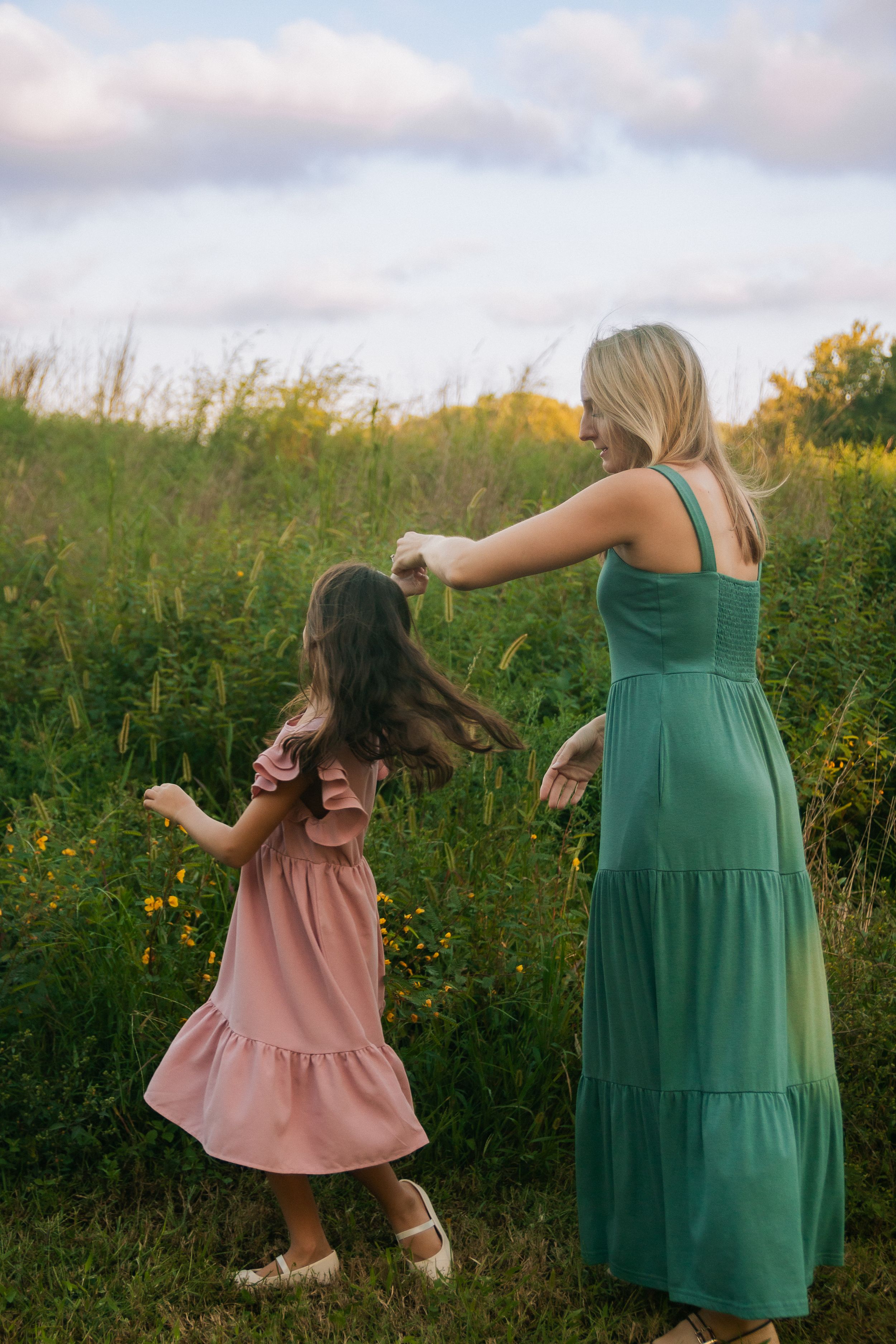 A pair in emerald green and pink dresses dance together in a sunlit meadow at golden hour.