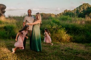 Family enjoying playful moments together in a sunlit meadow at sunset.