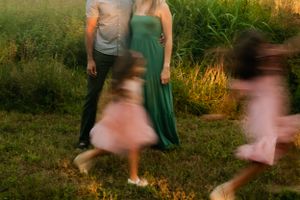 Motion-blurred figures in green and pink dresses twirl in a grassy field at dusk.