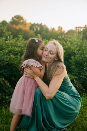 An intimate embrace between two people in green and pink dresses against a natural backdrop.