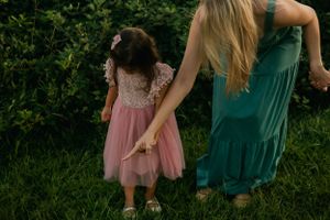 Two figures in coordinating green and pink dresses stand together in a lush garden setting.