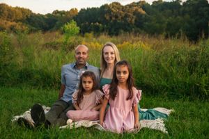 Family portrait in a lush green field with coordinated pink and grey outfits.