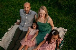 Family relaxes together on a woven blanket in an outdoor setting.