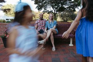 People gather on a brick wall seating area outdoors, with one person walking past in a motion blur.