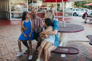 Group of people sitting at outdoor tables enjoying a sunny day at a casual restaurant patio.