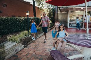 A group of people walk along a brick pathway near a red umbrella on a sunny afternoon.
