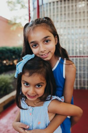 Two young children embrace and smile at the camera while wearing blue and striped outfits outdoors.