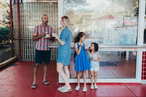 A group stands outside an establishment, with two adults and two children in blue and white outfits on a red floor.