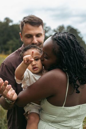 A tender family moment captured outdoors with gentle embraces and kisses against a natural background.