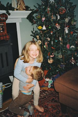 Decorated Christmas tree with ornaments and two children playing by couch on patterned rug.