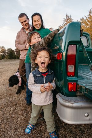Family posing together by vintage green pickup truck in autumn field.