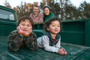 Three people laying in the bed of a green pickup truck on an autumn day, smiling and enjoying the outdoors together.