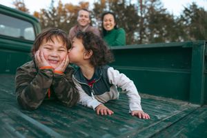 Family members share joyful moments together while laying in the back of a green pickup truck during autumn.