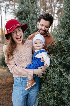 Family shares joyful moments together among evergreen trees on a sunny autumn day.