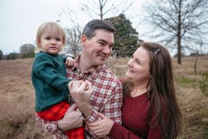 A family shares a joyful moment together outdoors on a winter day in a field with bare trees in the background.