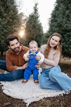 A family sits together on a blanket among evergreen trees during golden hour.