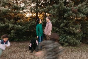 Family enjoying a sunset photoshoot in a forest setting with warm autumn colors and natural lighting.