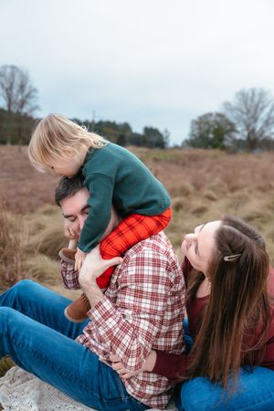 Couple in casual attire sharing playful moments together while relaxing outdoors in a field.