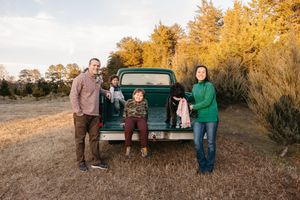 A group stands next to a vintage green pickup truck during golden hour in an autumn field setting.