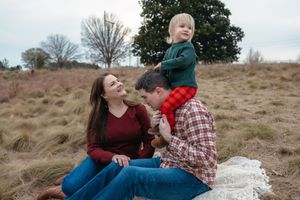 A couple sits together on a grassy hillside during an outdoor photoshoot session.