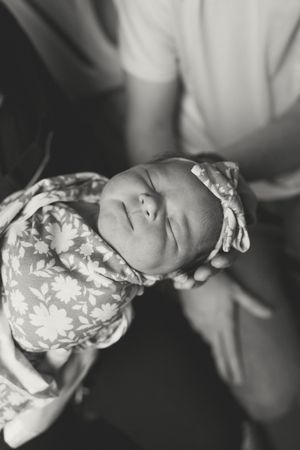 Black and white portrait of a sleeping newborn baby wearing a floral patterned outfit.