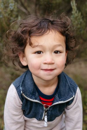 A series of close-up photos showing a young child with curly hair wearing a blue vest and white sleeves making playful expressions.
