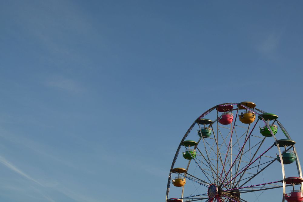 Colorful Ferris wheel against bright blue sky with vibrant passenger cars visible.