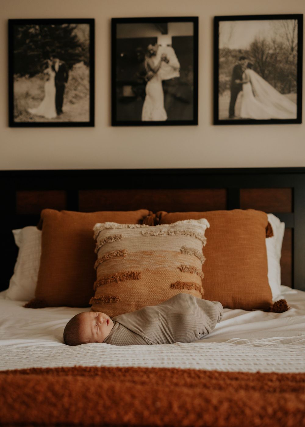 Newborn baby sleeping on bed with vintage wedding photos displayed on wall above.