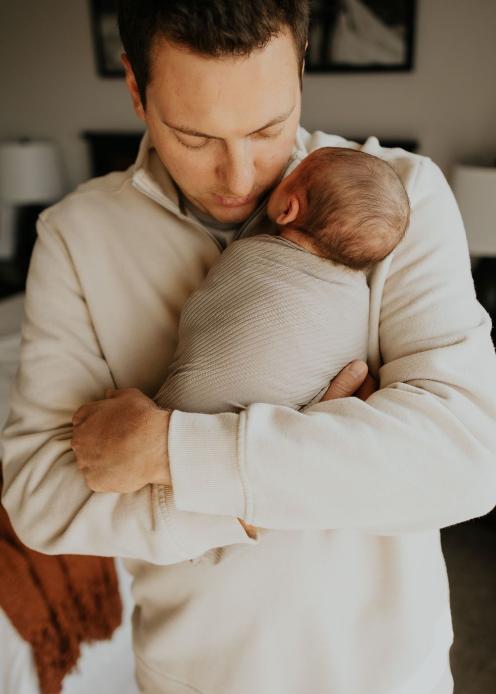 Tender moment between parent and newborn baby cuddled together in cozy white sweater.