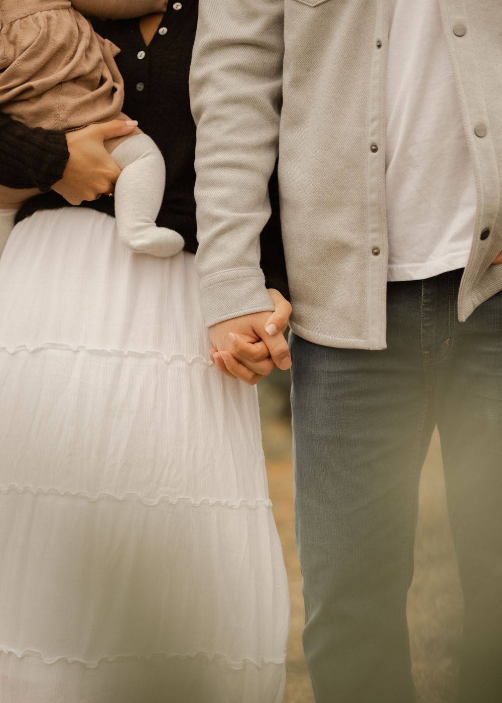 Cropped view of couple holding hands against white tulle dress and casual attire.