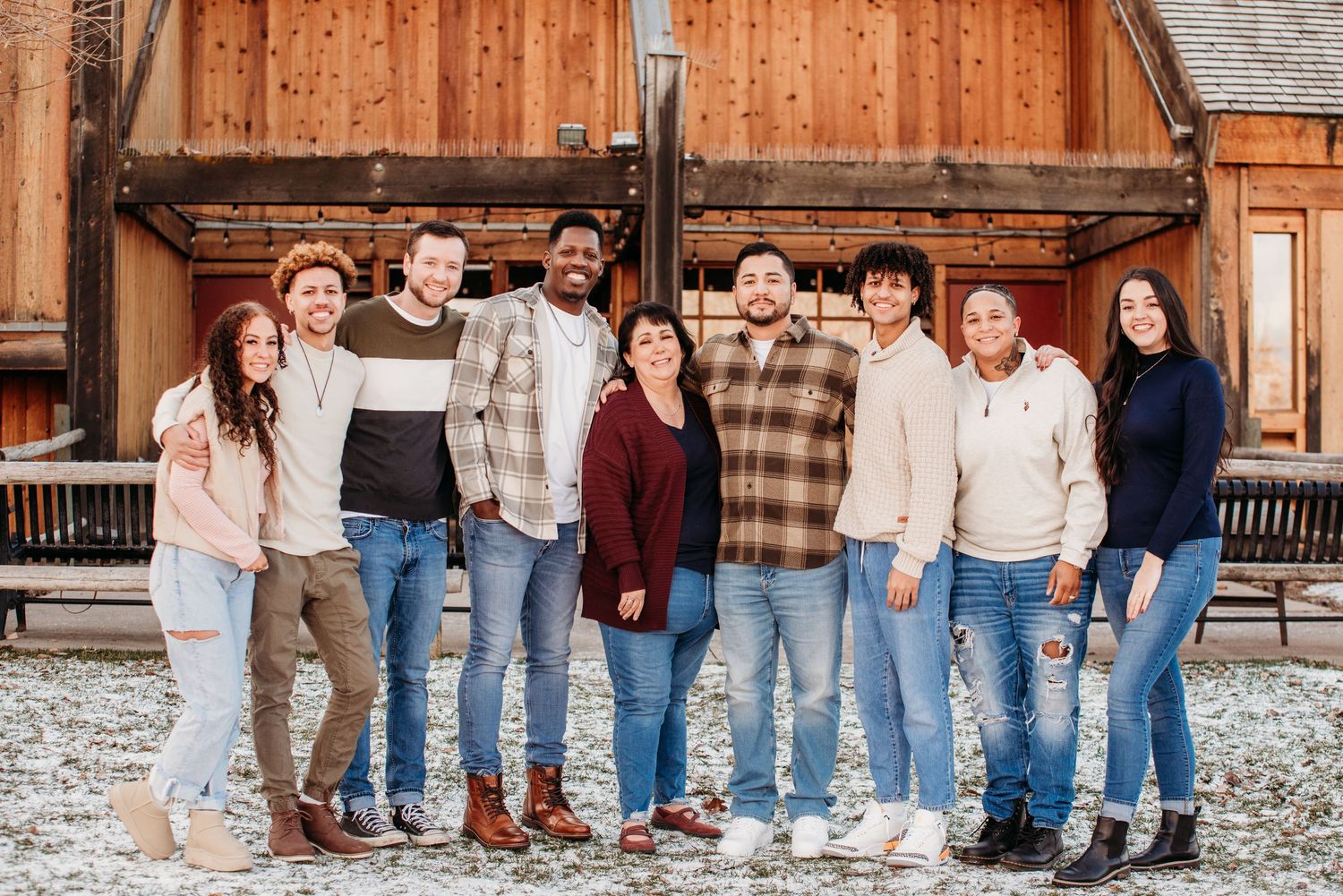 A group of people in casual winter attire posing together in front of a rustic wooden building.