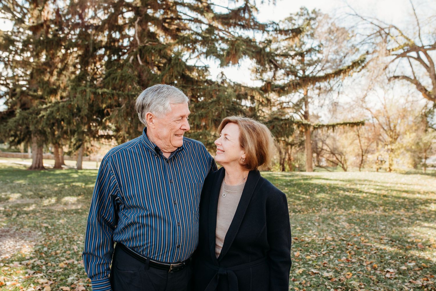 Couple sharing tender moment under evergreen trees in autumn park setting.