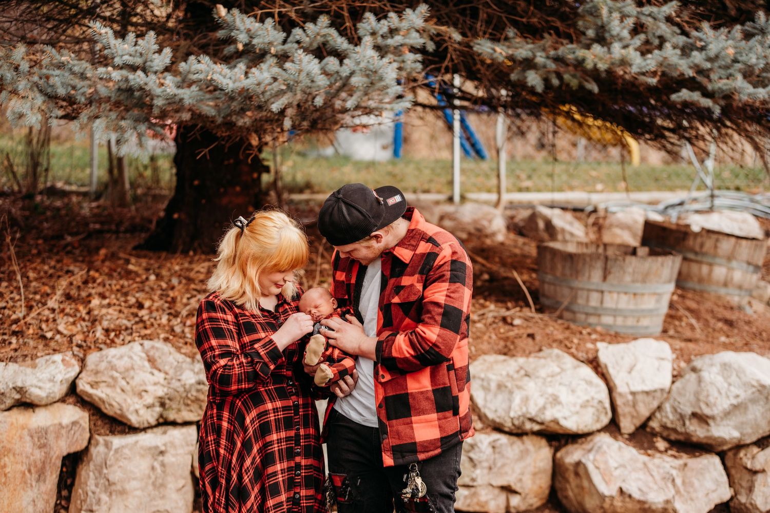 Two people in matching plaid shirts sharing an intimate moment by stone wall.