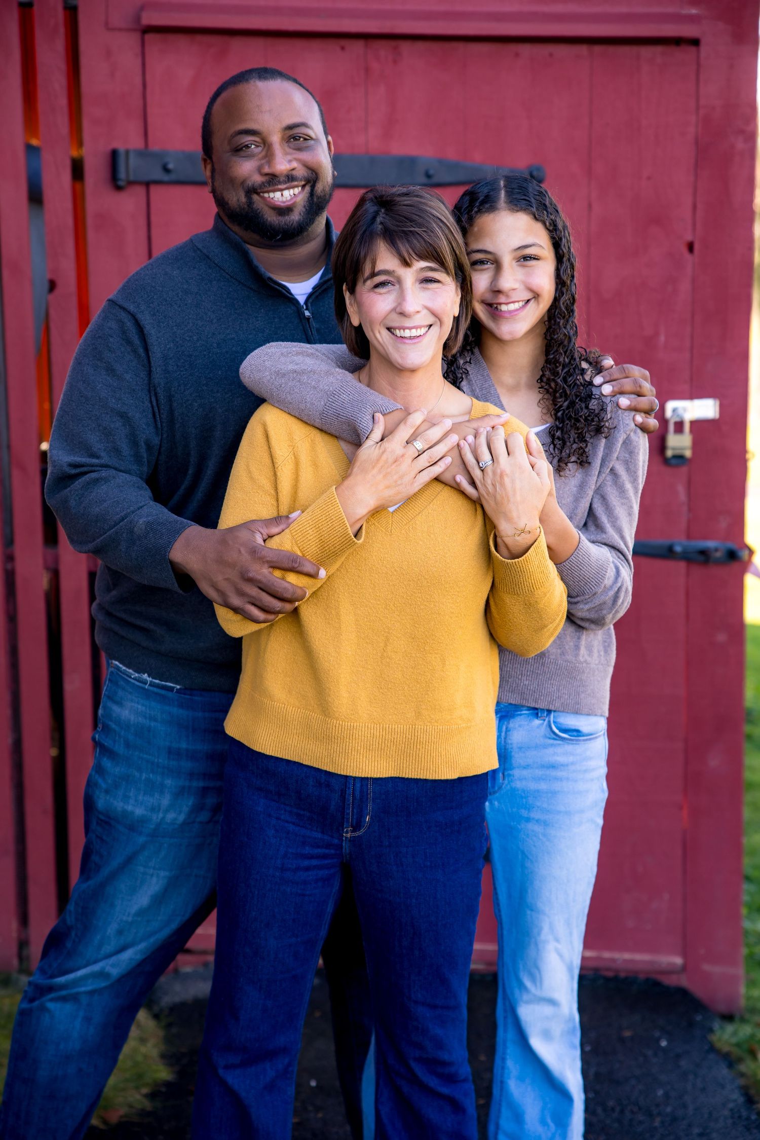 Family poses together on a wooden fence with autumn scenery in the background.