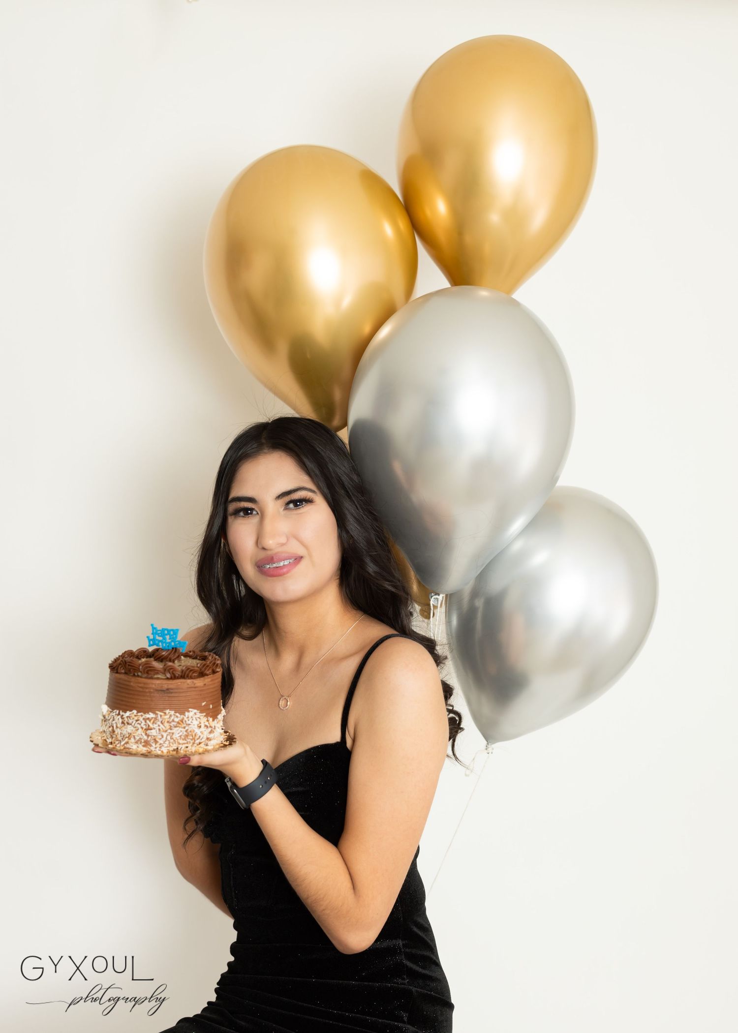 Festive portrait holding chocolate cake with metallic balloon backdrop.