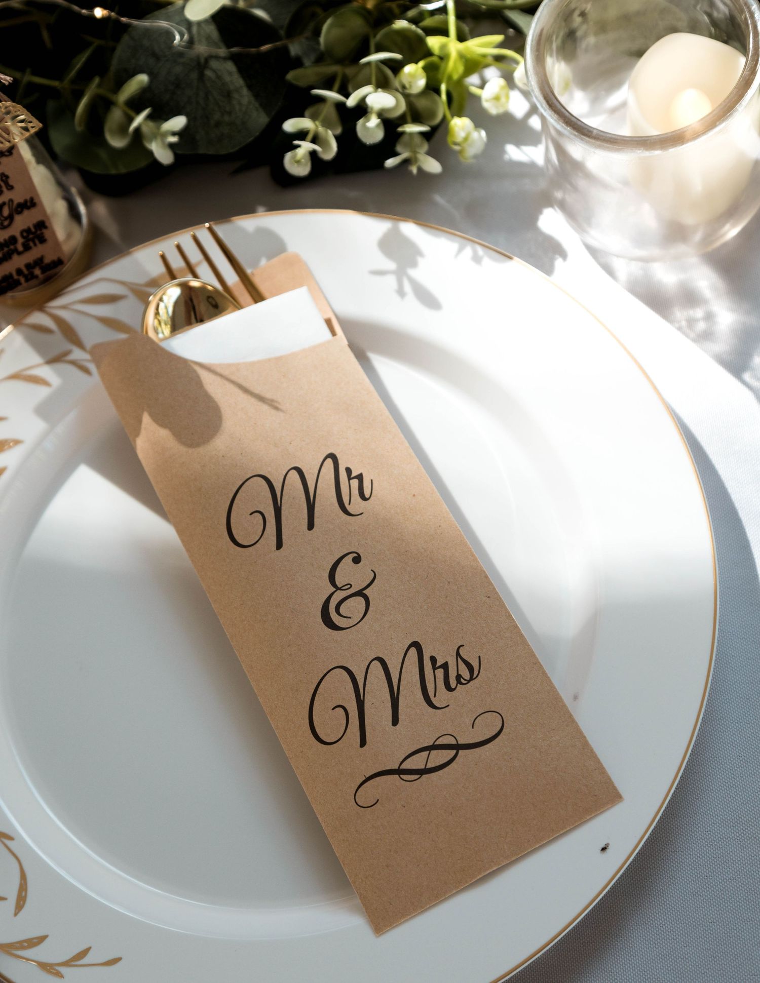 Elegant wedding place setting with kraft paper utensil holder marked 'Mr & Mrs' on white plate with floral decor.