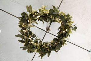 A decorative wreath made of green leaves and small yellow flowers arranged in a heart shape on a white background.